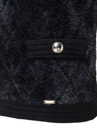 Schwarzer, strukturiert Stoff mit einer gerippten Taschenklappe, die mit einem glänzenden silbernen Knopf gesichert ist, sowie einem kleinen rechteckigen Metall-Label der Marke darunter.