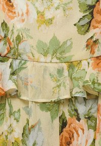 Bloemig jurkje van lichtgewicht gele stof met een groen en oranje rozenpatroon. De gerimpelde zoom voegt textuur en detail toe.