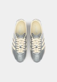 Grå og kremfargede joggesko med tre laterale striper, rund tå og snøring. Glatt tekstur og minimalistisk design. Ovenfra.