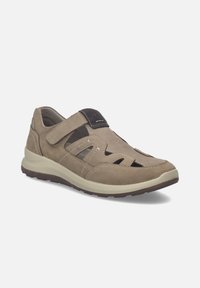 Chaussure décontractée pour homme de couleur brun clair avec bride velcro, détails ajourés, semelle rembourrée et bout arrondi sur fond blanc.