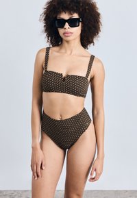 Biquíni preto e dourado com padrão, com um top cropped e calças de cintura alta. Apresenta alças grossas e um acabamento em tecido texturizado.