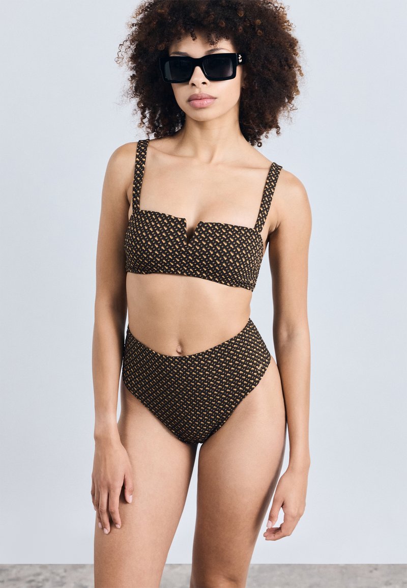 Biquíni preto e dourado com padrão, com um top cropped e calças de cintura alta. Apresenta alças grossas e um acabamento em tecido texturizado.