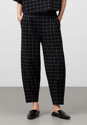 Zwart- en grijs geruite broek met een losse pasvorm, voorzien van plooien en zijzakken, gemaakt van een textuurstof. Gestoeld met donkere loafers.
