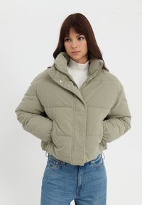 Ljusgrön kordflodspufferjacka med hög krage, tryckknappar, ribbad textur och två framfickor, bärs med blå jeans.