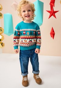 Tyrkysový sveter s veselými vzormi, vrátane Santy a stromčekov; doplnený o vyhrnuté modré džínsy a hnedé tenisky. Hravo geometrické pozadie.