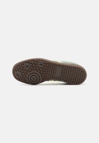 Green sneaker with brown rubber sole featuring textured grip, circular accents, and a brand logo. Crafted with a lightweight upper material.