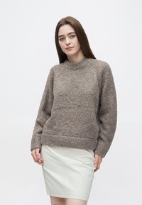 Brun stickad tröja med texturerat tyg, rund halsringning och långa ärmar, i kombination med en ljusfärgad pennkjol.