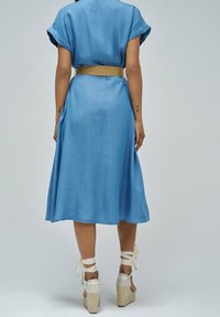 Jean jurk in lichtblauwe denim met korte opgerolde mouwen, een ceintuur in de taille en een uitlopende rok, gecombineerd met beige wedge sandalen.