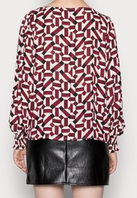 Langärmlige Bluse in Burgunderrot, Creme und schwarzem geometrischem Muster; mit elastischen Bündchen und abgerundetem Saum. Kombiniert mit einem schwarzen Minirock aus Leder.