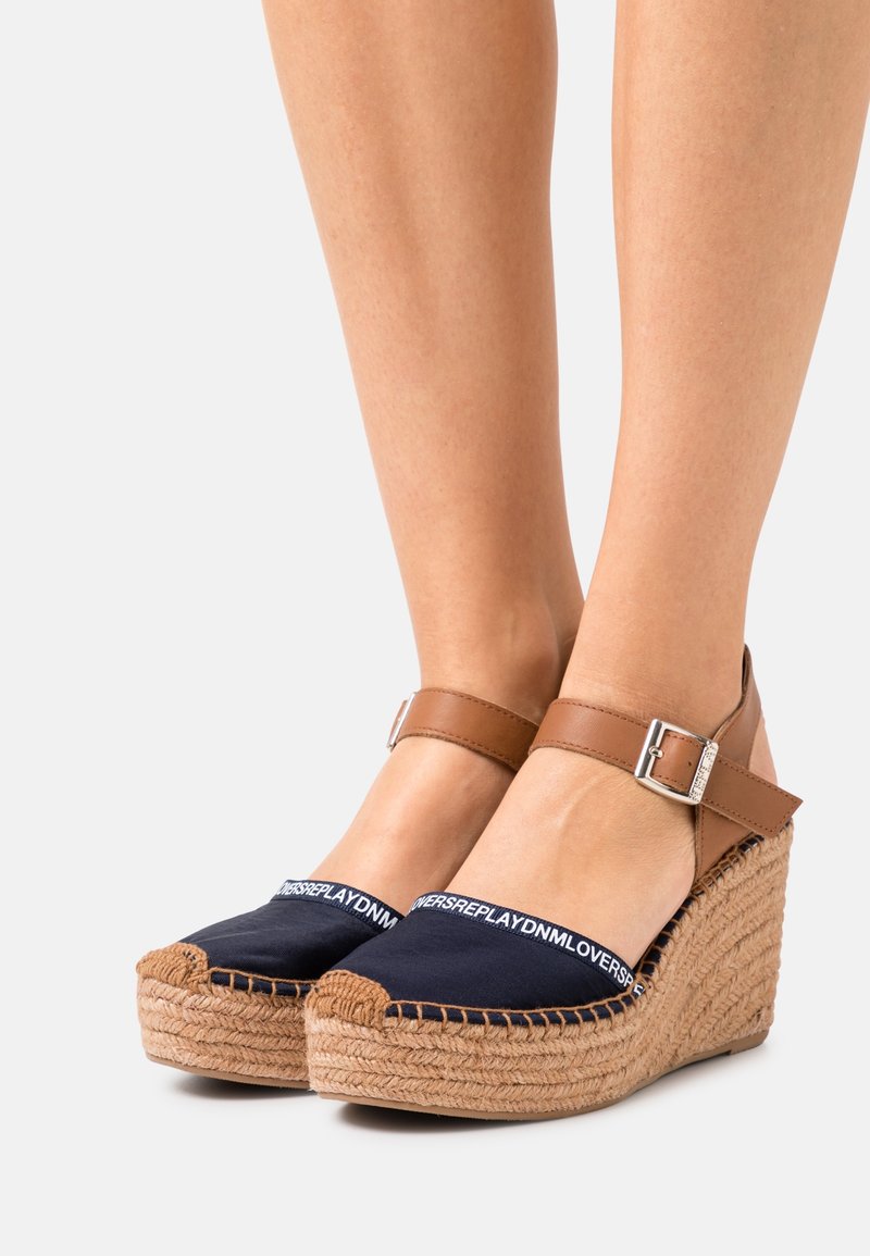 Espadrilles compensées avec une tige en toile bleu marine, une bride de cheville en cuir marron et une plateforme en corde naturelle. Elles présentent un détail cousu à lorteil.