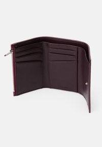 Πορτοφόλι από μπορντό δέρμα, με πολλές θήκες για κάρτες, θήκη με φερμουάρ, λεία υφή και λογότυπο αποτυπωμένο στο εσωτερικό.