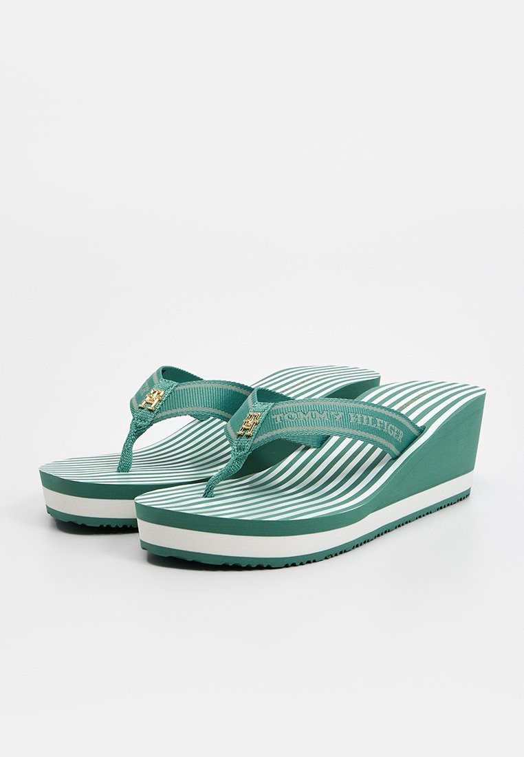 Sandales compensées rayées vertes avec une semelle texturée, des brides en caoutchouc et un accent en logo doré sur la bride. Présente un design superposé.