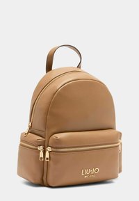 Zaino in pelle marrone con forma arrotondata, due tasche con zip e accessori in tonalità oro. Presenta il logo del marchio in rilievo nella parte anteriore.