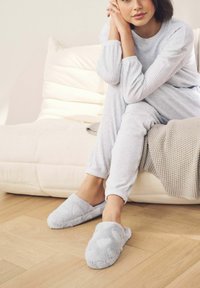 Šedé chlpate papuče srdiečkového vzoru, vyrobené z mäkkého materiálu. Dizajn obsahuje slip-on štýl, v kombinácii s ľahkým rebrovaným domácim oblečením.
