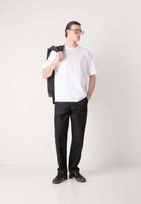 Hvit kortermet t-skjorte, mørke denim bukser, grå jakke lagt over skulderen, solbriller, uformelt fottøy, minimalistisk design.