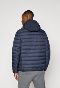 Námornícky modrá páperová bunda so zipsom vpredu, horizontálnym prešívaním a priliehavou kapucňou. Materiál je hladký a lesklý s jemným leskom.