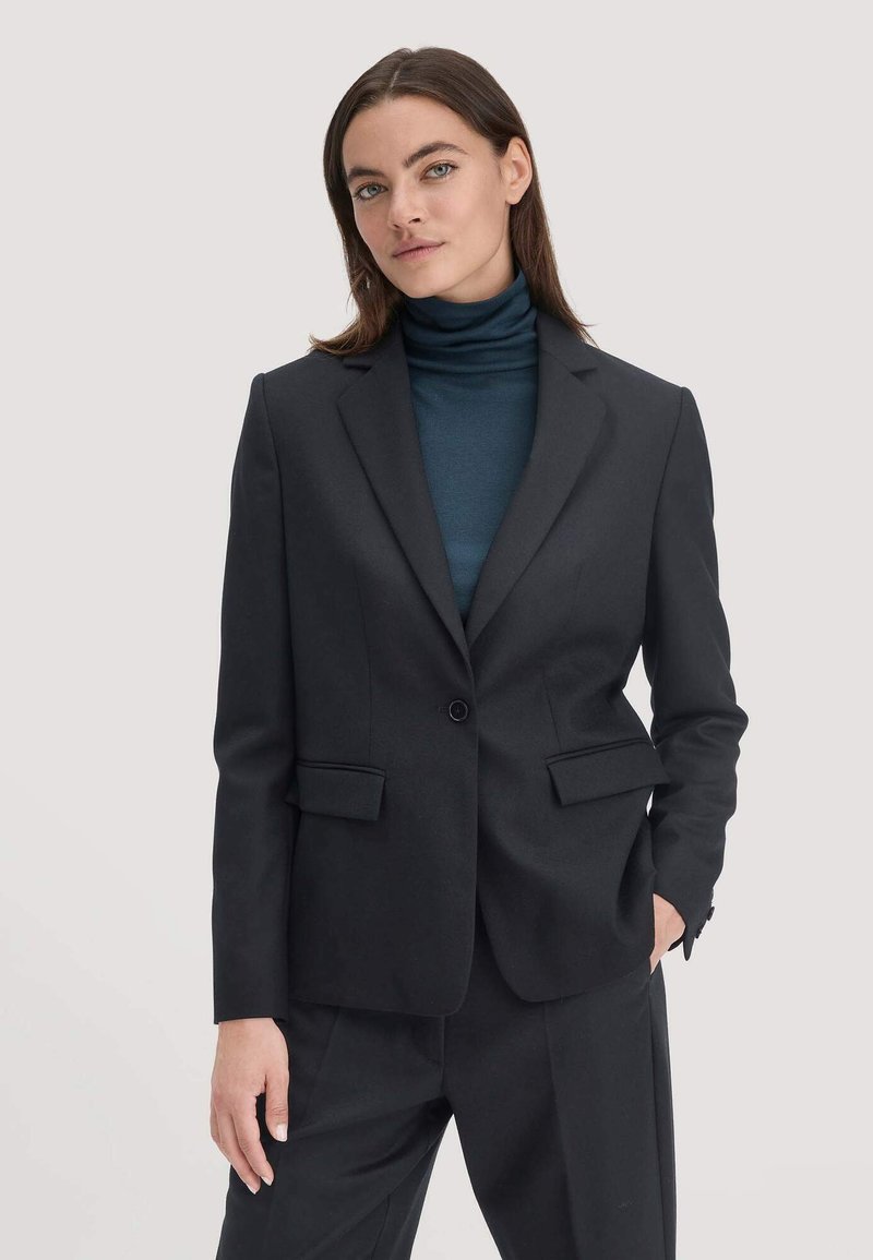 Zwarte op maat gemaakte blazer met enkele knoopsluiting, notch revers, twee voorkruiken, gecombineerd met een donkere coltrui. Glad materiaal en gestructureerde pasvorm.