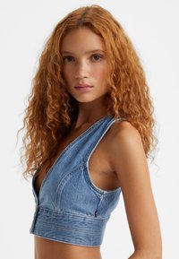 Denim top, gaisā zila, dziļa V veida kakla izgriezums, bez piedurknēm, pieguļošs siluets, redzamas šuves un pogu aizdare priekšā.