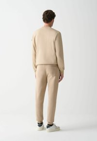 Sudadera beige y joggers a juego, tejido suave, corte moderno, puños acanalados, diseño minimalista, pequeño logo en la manga de la sudadera.