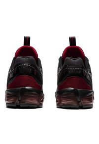Scarpe sportive nere con parte superiore in rete, accenti rossi, collare imbottito e suola nera e rossa testurizzata con un motivo geometrico.