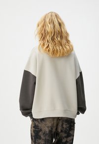 Sudadera de gran tamaño en gris claro y gris oscuro con mangas anchas y el dobladillo acanalado. Tejido suave y diseño minimalista, sin patrones adicionales.
