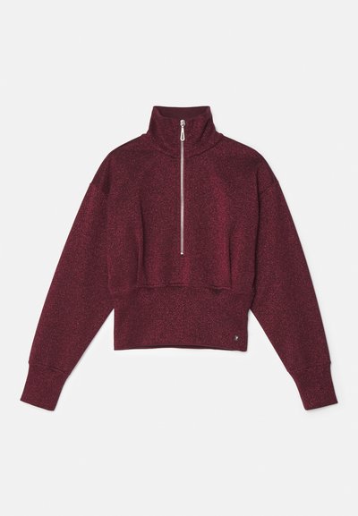 Burgundijska skrajšana kapuca s visokim ovratnikom, polnim zadrgo in ohlapnimi rokavi. Tkanina ima rahlo sijoč videz in mehak otip.