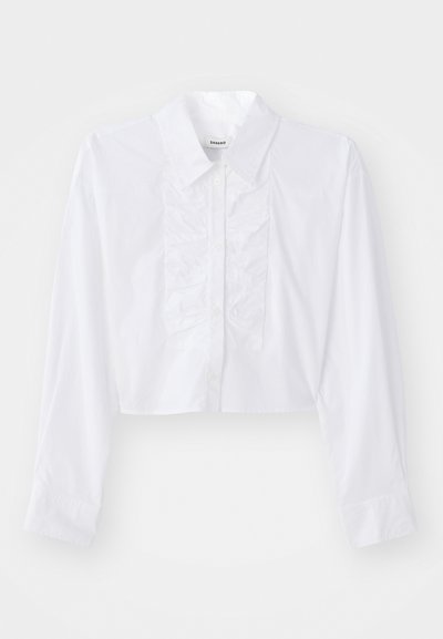 Chemise blanche raccourcie en coton lisse, avec un détail froncé sur le devant, un col pointu, et des manches longues avec des poignets boutonnés.