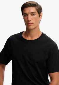 Sort bomulds-T-shirt med rund halsudskæring og korte ærmer. Har subtil logo-broderi på brystet, glat tekstur og almindelig pasform.