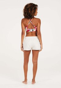 Reggiseno sportivo floreale dai colori vivaci con spalline incrociate, abbinato a pantaloni corti bianchi con vita elastica, mostrato di spalle.