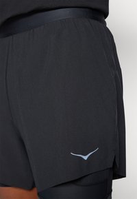 Shorts negri de atletism, realizate dintr-un material ușor. Au o talie tonală și un mic logo albastru pe partea stângă.