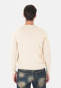 Maglione lavorato a maglia beige chiaro con polsini e orlo a coste, scollo rotondo e vestibilità morbida, abbinato a jeans blu sbiaditi.