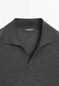 Col polo en tricot gris foncé avec une étiquette noire portant l'inscription « Massimo Dutti Made in China » à l'intérieur de l'encolure.