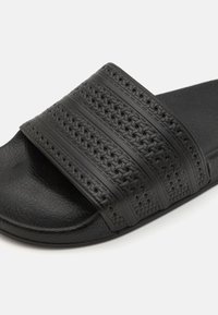 Sorte slip on sandaler med en struktureret rem, der har tre hævede linjer. Fremstillet af gummi, med en mat overflade og en tyk sål.