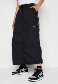 Svart sportkjol med lös design, elastisk midja och dragsko. Har vita sidosträck och en liten Nike-logotyp. Buren med höga svarta sneakers.