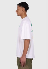 Hvid kortærmet t-shirt med rund hals. Har trykt grøn og gul tekst på ryggen. Blødt bomuldsstof med en afslappet pasform.