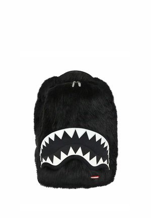 Mochila negra peluda con un bolsillo delantero que presenta un diseño de dientes de tiburón blancos y dos cremalleras plateadas.