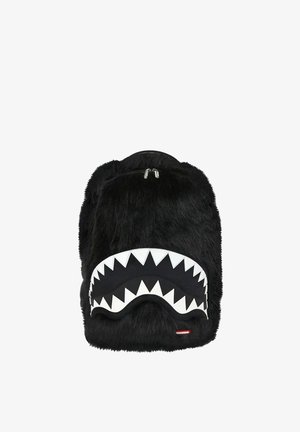 Mochila negra peluda con un bolsillo delantero que presenta un diseño de dientes de tiburón blancos y dos cremalleras plateadas.