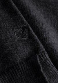 Zwart gebreid sweater met een zachte textuur, voorzien van een klein geborduurd hartaccent nabij de naad. Voornamelijk glad met ribbelranden.