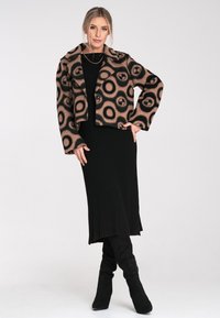 Krótką kurtkę z miękkiego, wzorzystego materiału w okrągłe wzory w kolorze czarnym i beżowym; zestawioną z czarną sukienką w prążki i czarnymi botkami za kostkę.