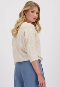 Beige geribde trui met driekwartmouwen, zachte textuur en een relaxte pasvorm, gecombineerd met lichtblauwe wijde broek.