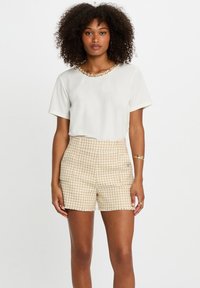 Hvit kortermet topp med teksturert krage, kombinert med høyt liv shorts i beige hundtannmønster med lommer og diskret hardware.