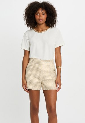Top bianco a maniche corte con collare strutturato, abbinato a pantaloni corti a vita alta in fantasia houndstooth beige con tasche e dettagli in metallo discreti.