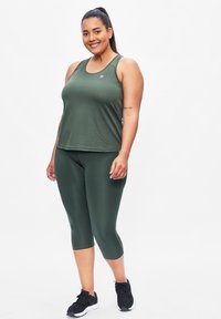 Groene sportieve tanktop met een ronde halslijn, gecombineerd met bijpassende capri leggings. Zwarte sportschoenen met een gestructureerd ontwerp.