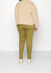 Chaqueta de forro polar beige con un corte relajado, combinada con pantalones de tiro ajustado en verde oliva. El conjunto incluye zapatos con suela gruesa blanca.