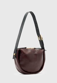 Bolsa de couro burgundy com uma forma arredondada, alça preta ajustável, detalhes em dourado e fecho em zíper. Os acentos pretos na alça aprimoram o design.