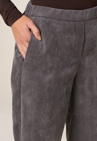 Pantalones de pana grises con textura de ribete vertical, que incluyen bolsillos laterales y una cinturilla elástica. La tela tiene un acabado mate suave.