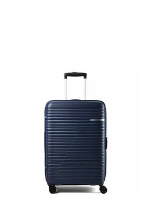 Valise rigide bleu marine avec des rainures horizontales, quatre roues et une poignée télescopique noire déployée verticalement.