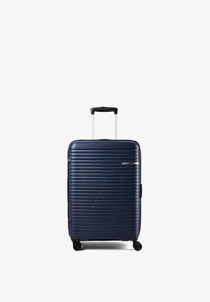 Valigia rigida blu navy con scanalature orizzontali, quattro ruote e manico telescopico nero esteso in posizione verticale.