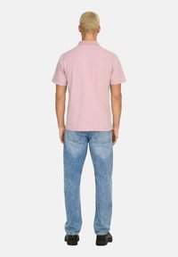 Camisa polo de color rosa claro con cuello, mangas cortas y un diseño sencillo, combinada con jeans de pierna recta de color azul claro y zapatos negros.