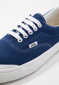 Blaue Wildledersneaker mit weißen Schnürsenkeln, featuring ein gesticktes Design und ein Vans-Logo-Tag an der Seite. Weiße Gummisohle.